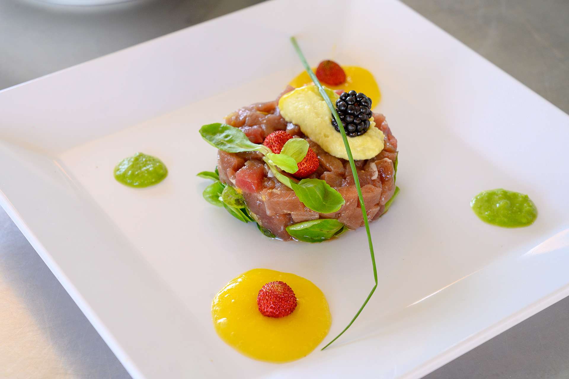 Tartare di tonno con frutti di bosco, erba cipollina e salse colorate su piatto bianco