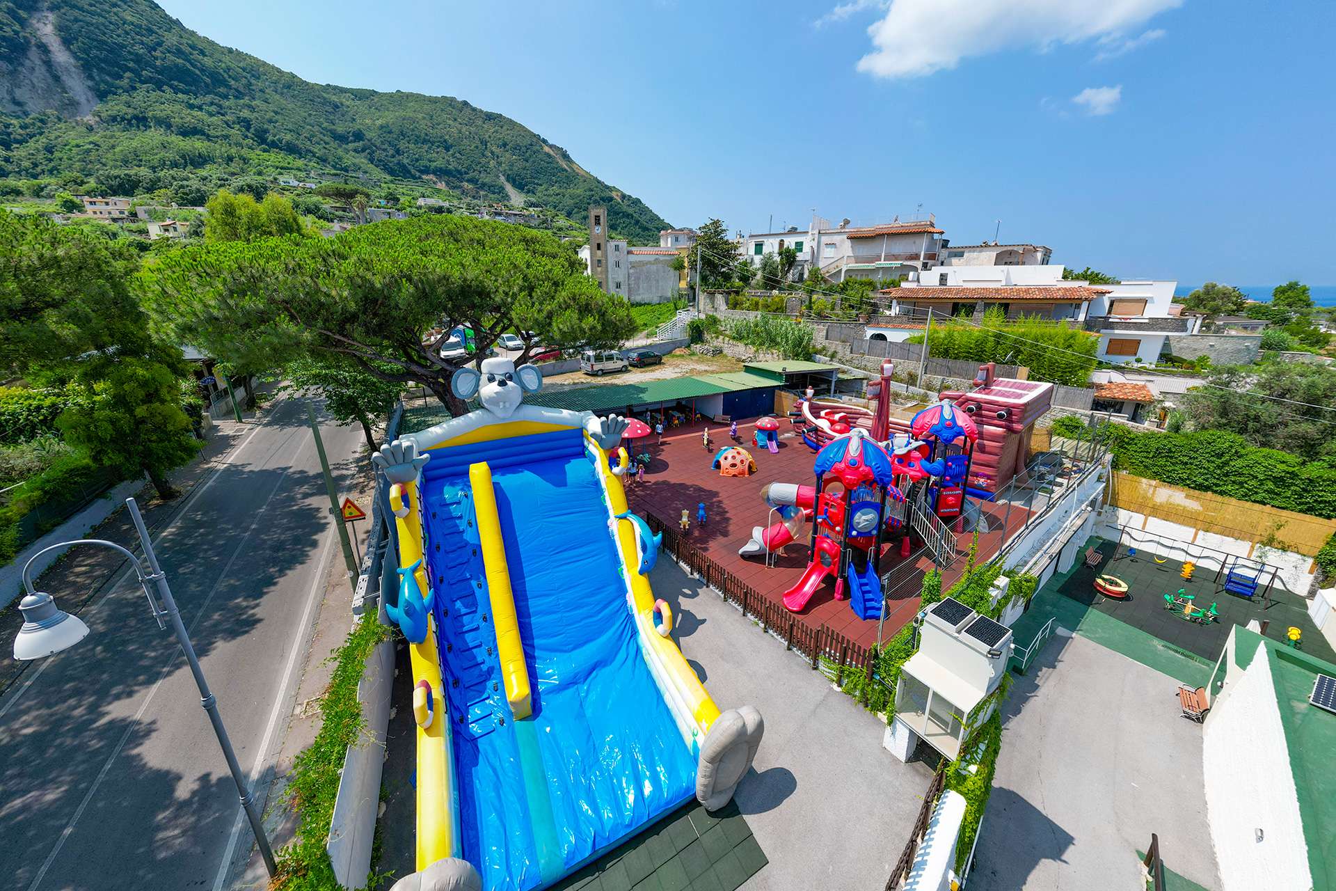 Veduta dall'alto di Mikyland: grande scivolo gonfiabile, parco giochi e giardino con pini